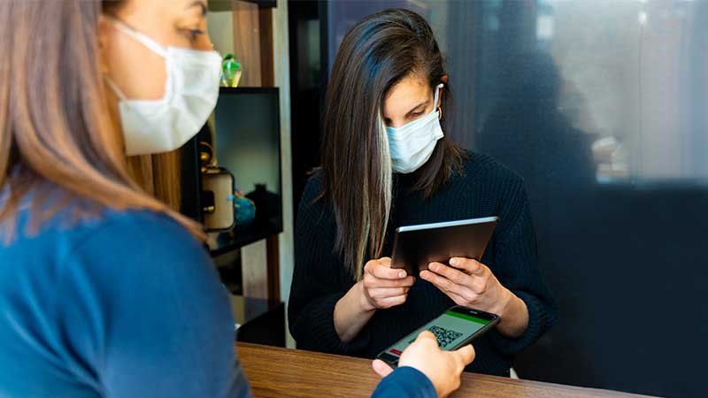 Pessoa de máscara ao balcão numa entrada de uma discoteca mostra o certificado digital covid